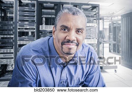 Stock Image - Mixed race businessman sitting in server room. Fotosearch