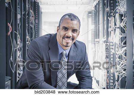 Mixed race businessman sitting in server room View Large Photo Image Stock Photo - Mixed race businessman sitting in server room. Fotosearch