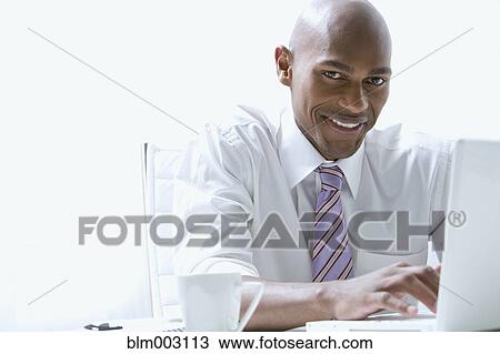 Stock Image - Mixed race businessman using laptop at desk. Fotosearch