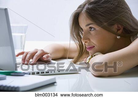 Picture - Mixed race businesswoman laying on desk using laptop. Fotosearch