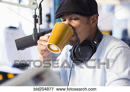Stock Photo - Mixed race disc jockey drinking cup of coffee in studio. Fotosearch