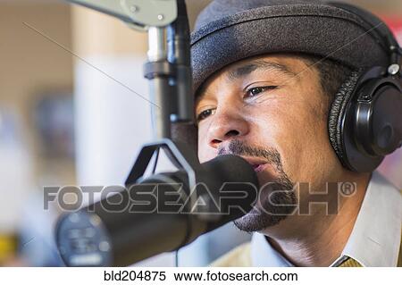 Stock Photography - Mixed race disc jockey talking into mic in studio. Fotosearch