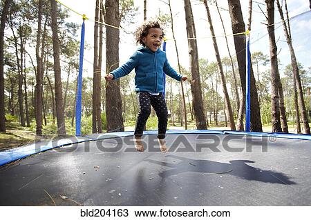 Stock Image - Mixed race girl jumping on trampoline. Fotosearch