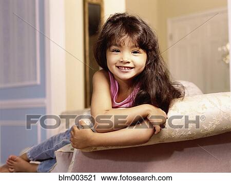 Stock Image - Mixed race girl leaning over edge of sofa. Fotosearch
