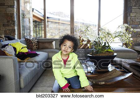 Stock Photo - Mixed race girl sitting on coffee table. Fotosearch