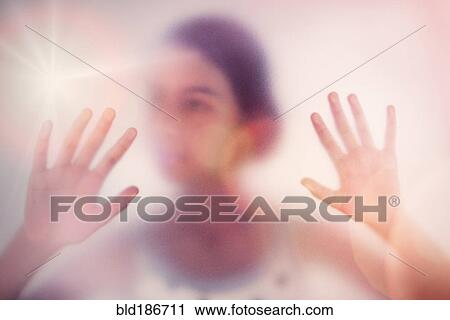 Stock Image - Mixed race girl standing behind frosted glass. Fotosearch