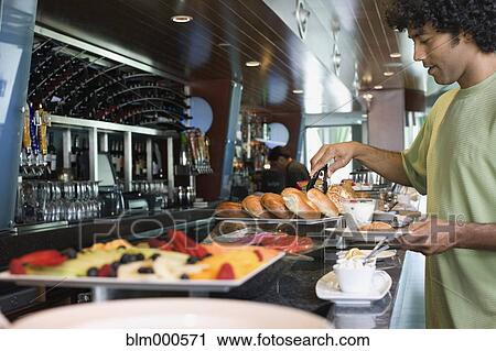 Stock Image - Mixed race man choosing food from breakfast buffet. Fotosearch