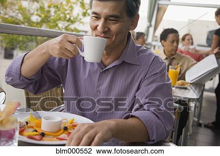 Stock Image - Mixed race man drinking coffee in restaurant. Fotosearch