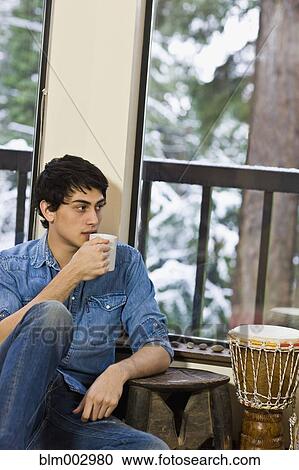 Mixed race man drinking coffee in living room View Large Photo Image Stock Image - Mixed race man drinking coffee in living room. Fotosearch