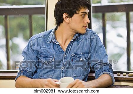 Stock Image - Mixed race man drinking coffee in living room. Fotosearch
