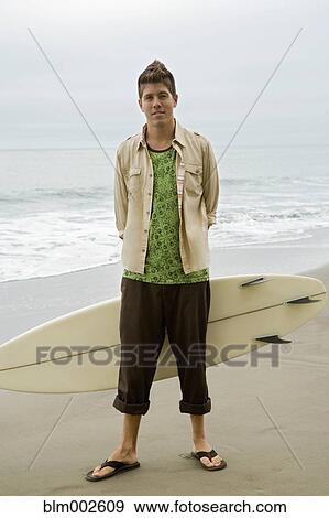 Stock Photo - Mixed race man holding surfboard. Fotosearch