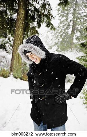 Stock Image - Mixed race man in hooded coat outdoors in snowfall. Fotosearch