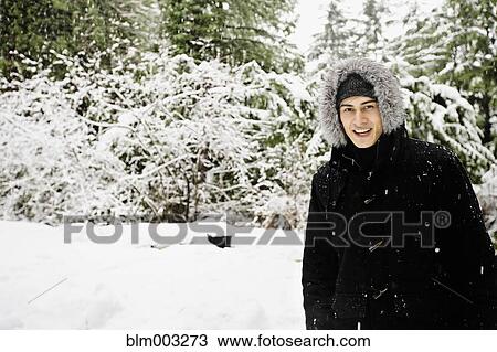 Stock Image - Mixed race man in hooded coat outdoors in snowfall. Fotosearch