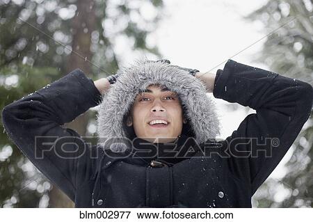 Stock Photo - Mixed race man in hooded coat outdoors in snowfall. Fotosearch