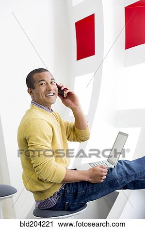 Mixed race man on laptop talking on cell phone View Large Photo Image Stock Image - Mixed race man on laptop talking on cell phone. Fotosearch