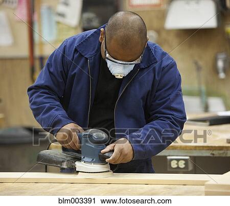 Stock Image - Mixed race man sanding in workshop. Fotosearch