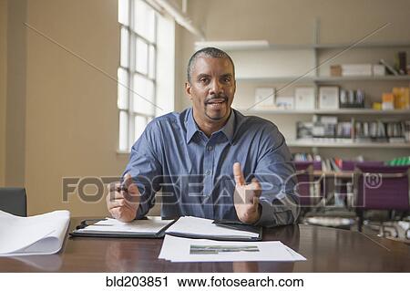 Stock Image - Mixed race man talking at desk. Fotosearch