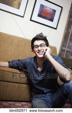 Stock Image - Mixed race man talking on cell phone in living room. Fotosearch