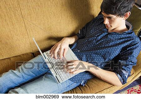 Stock Photo - Mixed race man typing on laptop on sofa. Fotosearch