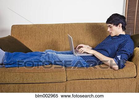 Mixed race man typing on laptop on sofa View Large Photo Image Stock Photography - Mixed race man typing on laptop on sofa. Fotosearch