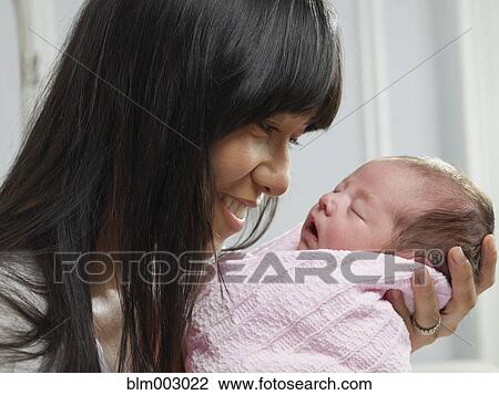 Stock Image - Mixed race mother cuddling newborn baby. Fotosearch