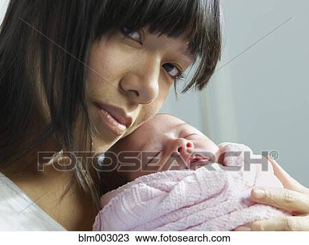 Stock Image - Mixed race mother cuddling newborn baby. Fotosearch