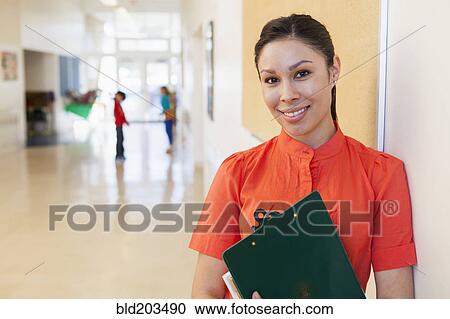 Mixed race teacher holding clipboard in school hallway View Large Photo Image Stock Image - Mixed race teacher holding clipboard in school hallway. Fotosearch