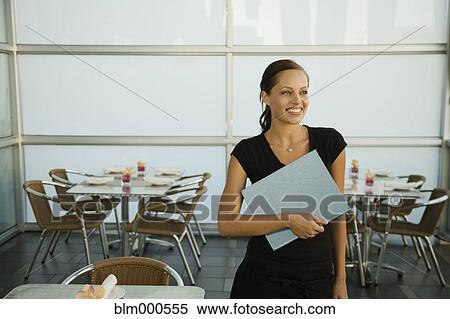 Stock Photography - Mixed race waitress holding menu in restaurant. Fotosearch