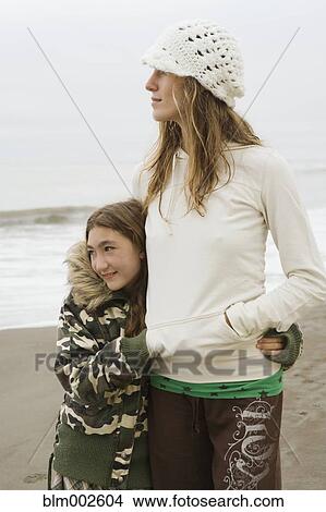 Picture - Mixed race woman and sister hugging at beach. Fotosearch