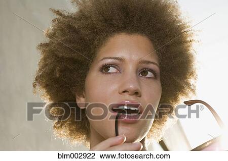 Stock Image - Mixed race woman biting on sunglasses. Fotosearch