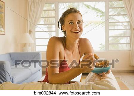 Picture - Mixed race woman eating cereal in living room. Fotosearch