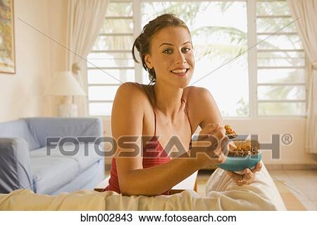 Stock Image - Mixed race woman eating cereal in living room. Fotosearch