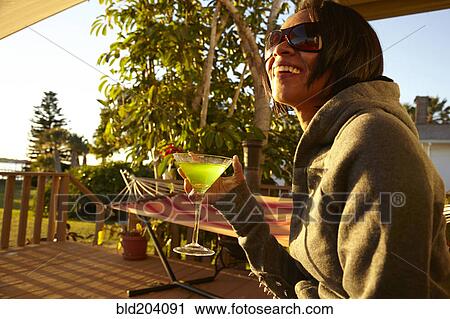 Stock Image - Mixed race woman having cocktail on porch. Fotosearch
