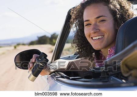 Stock Photo - Mixed race woman holding binoculars in convertible. Fotosearch
