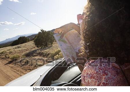 Stock Photography - Mixed race woman holding map on dirt road. Fotosearch