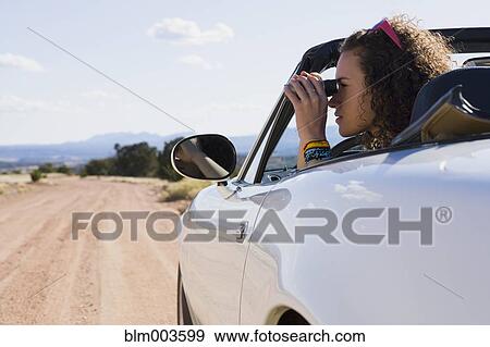 Stock Photo - Mixed race woman in convertible looking through binoculars. Fotosearch