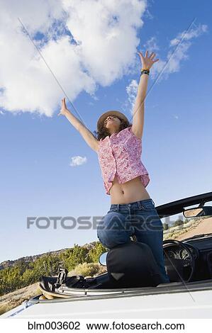 Stock Image - Mixed race woman in convertible with arms raised. Fotosearch