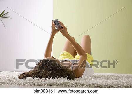 Stock Image - Mixed race woman laying on floor looking a cell phone. Fotosearch