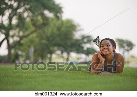 Picture - Mixed race woman laying on grass using cell phone. Fotosearch