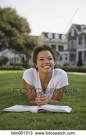 Stock Image - Mixed race woman laying on grass with book. Fotosearch