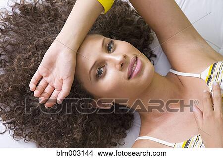 Picture - Mixed race woman laying with arm over forehead. Fotosearch