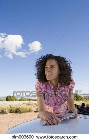 Stock Image - Mixed race woman leaning on car and holding map. Fotosearch