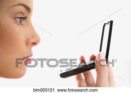 Stock Image - Mixed race woman looking at reflection in compact mirror. Fotosearch