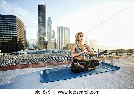 Stock Image - Mixed race woman meditating on urban rooftop. Fotosearch