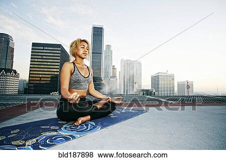 Stock Photo - Mixed race woman meditating on urban rooftop. Fotosearch