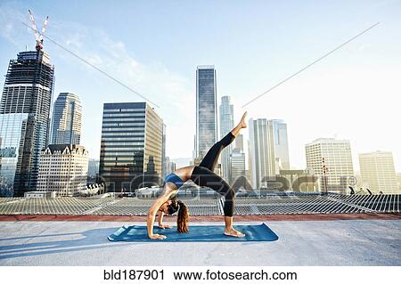 Stock Image - Mixed race woman practicing yoga on urban rooftop. Fotosearch