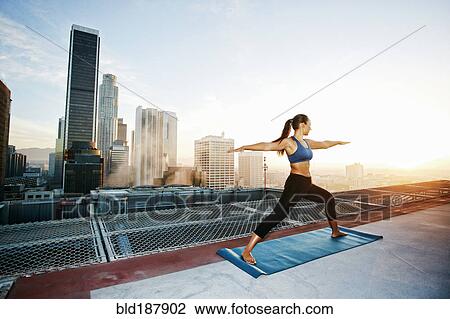 Stock Image - Mixed race woman practicing yoga on urban rooftop. Fotosearch