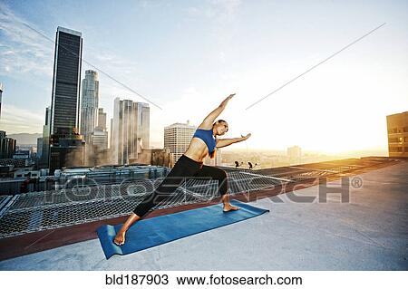 Stock Image - Mixed race woman practicing yoga on urban rooftop. Fotosearch
