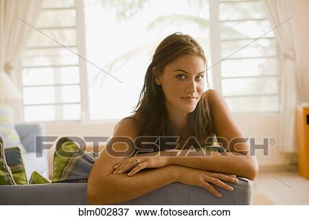 Stock Photo - Mixed race woman sitting on sofa in living room. Fotosearch