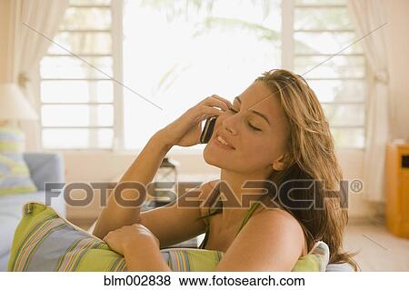 Mixed race woman sitting on sofa in living room talking on cell phone View Large Photo Image Stock Photo - Mixed race woman sitting on sofa in living room talking on cell phone. Fotosearch